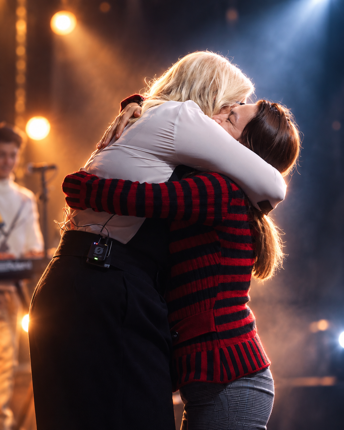 Dos personas abrazadas en el escenario en un momento emocional del concierto, fotografía oficial en vivo